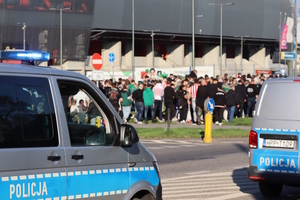 Radiowozy stojące przy stadionie. W tle tłum kibiców