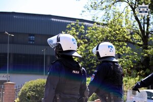 Dwoje policjantów prewencji Policji ubranych w kaski oraz odzież ochronną stojących na tle stadionu.