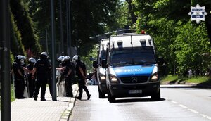 Oznakowane radiowozy  policji, w pobliżu stoją policjanci w umundurowaniu oraz kaskach ochronnych.