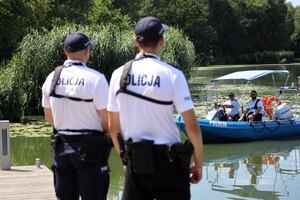 Umundurowani policjanci patrolu rowerowego. W tle widoczna łódź motorowa Policji wodnej.