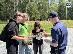 Umundurowany policjant rozdający gadżety grupie młodzieży.