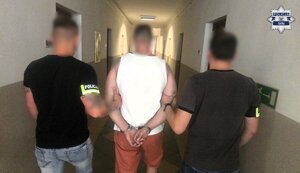 Nieumundurowani policjanci operacyjni prowadzą zatrzymanego, który ma założone kajdanki.