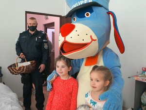Sznupek pozuje do zdjęcia z dwiema dziewczynkami, obok stoi policjant z koszem w którym są słodycze