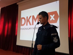 umundurowany policjant stoi na scenie, za sobą na wyświetlaczu widać logo fundacji DKMS