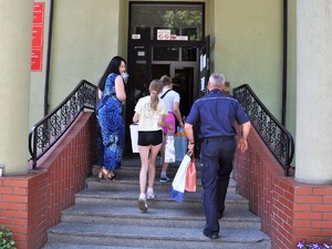 po schodach do budynku wchodzą dziewczynki, kobieta i policjant, wszyscy niosą torby prezentowe w rękach
