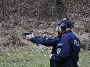 obok policjanta, który kieruje broń w stronę tarczy stoi drugi policjant, obserwuje jego trening strzelecki