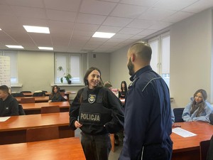 uczennica ubrana w kamizelkę kuloodporną uśmiecha się do policjanta