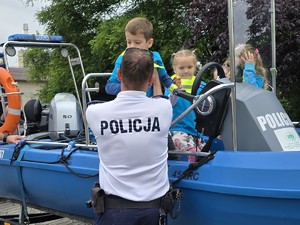 uczestnicy festynu profilaktycznego stoją przy policyjnym stanowisku, gdzie znajduje się policyjna łódź