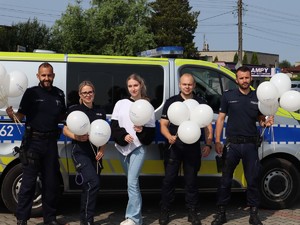 policjanci stoją przed radiowozem, trzymają balony