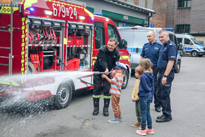 Policjanci, strażak i mały chłopiec przy wozie bojowy straży pożarnej.