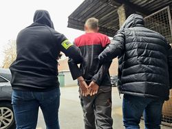 na zdjęciu policjanci prowadzą zatrzymanego mężczyznę