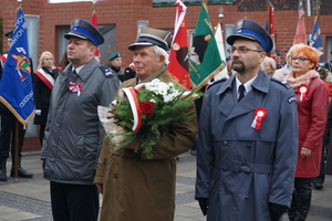 Delegacja składająca wiązankę kwiatów przez tablicą poległych w walczące o niepodległość.