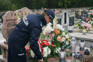 Naczelnik Wydziału Doboru i Szkolenia Komendy Wojewódzkiej Policji w Katowicach poprawia wstęgi położonych na grobie kwiatów.