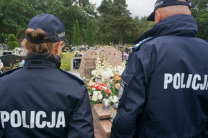 Widoczni stojący policjanci, a pomiędzy nimi w tle grób zmarłego policjanta.