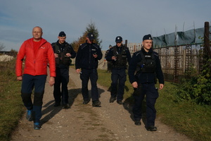 Na zdjęciu widoczni umundurowani policjanci, którzy obsługując urządzenia GPS idą drogą wraz z ratownikiem