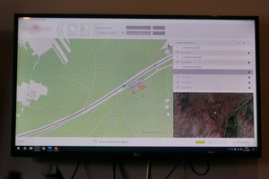 Na zdjęciu widoczny wyświetlony na ekranie telewizora slajd, przedstawiający mapę i realne zdjęcie terenu zrobione z lotu ptaka.