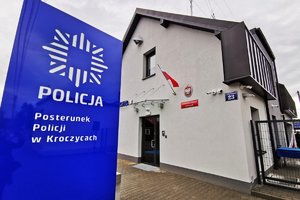 Na zdjęciu widoczny budynek Posterunku Policji w Kroczycach, przed którym znajduje się panel informacyjny. Na niebieskim tle, znaduje się biała gwiazda policyjna i napis Policja, a poniżej napis: Posterunek Policji w Kroczycach.