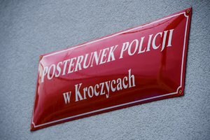 Na zdjęciu widoczna czerwona tabliczka na murze budynku, na której widnieje biały napis: Posterunek Policji w Kroczycach