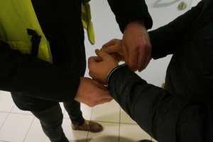 Na zdjęciu widoczne ręce zatrzymaneg o mężczyzny, na które zkaładne są kajdanki.