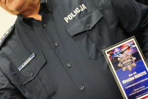 Zdjęcie kolorowe. Widoczny na nim częściowo aspirant sztabowy Mirosław Marczyk trzymający pamiątkową statuetkę. Na koszuli służbowej widoczny imiennik z jego nazwiskiem.