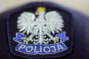 Na kolorowym zdjęciu widoczna naszywka na policyjnej czapce - orzeł w koronie, a pod nim niebieska wstęga z napisem POLICJA.
