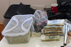 Widoczna marihuana w plastikowym pudełku leżącym na stole. Obok znaczna ilość banknotów.