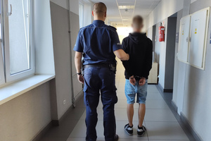 Policjant prowadzi korytarzem zatrzymanego nastolatka.