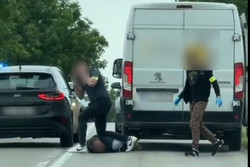 Na zdjęciu widoczny dostawczy samochód oraz nieoznakowany radiowóz. Widoczna też osoba leżąca na ziemi i trzymający ją nieumundurowany policjant.