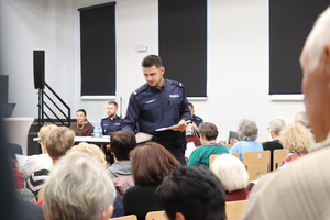 Na zdjęciu widoczny policjant, który rozdaje ankiety uczestnikom debaty.