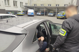 Na zdjęciu widoczny nieumundurowany policjant z opaską na ramieniu z napisem POLICJA oraz siedzącego w nieoznakowanym radiowozie mężczyznę.