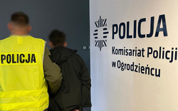Na zdjęciu widoczny nieumundurowany policjant w kamizelce odblaskowej z napisem Policja oraz zatrzymany mężczyzna.