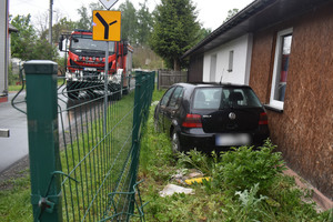 Na zdjęciu widoczny samochód osobowy, który stoi na zieleni pomiędzy ogrodzeniem a domem.