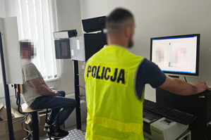 Na zdjęciu widoczny technik kryminalistyki, który robi zdjęcia sygnalityczne zatrzymanemu mężczyźnie.