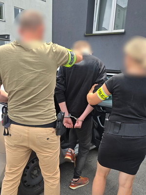 Na zdjęciu widoczna nieumundurowani policjantka i policjant oraz zatrzymany mężczyzna, który wsiada do nieoznakowanego radiowozu.