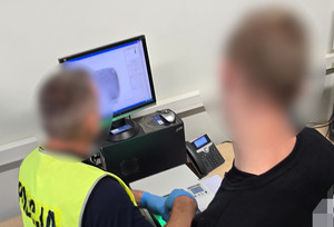 Na zdjęciu widoczny technik kryminalistyki i zatrzymany mężczyzna, któremu skanuje linie papilarne.