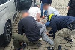 Na zdjęciu widoczni nieumundurowani policjanci podczas zatrzymania mężczyzny. Mężczyzna leży na ziemi i przytrzymują go policjanci.