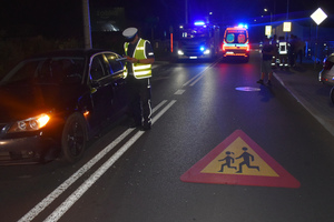 Na zdjęciu widoczne miejsce zdarzenia drogowego - policjant wykonujący czynności, ambulans i wóz strażacki.