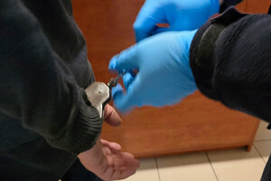 Na zdjęciu widoczne ręce zatrzymanego mężczyzny, na które policjant zakłada kajdanki.