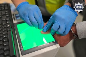 Na zdjęciu widoczne dłonie mężczyzny podczas skanowania linii papilarnych przez technika kryminalistyki.