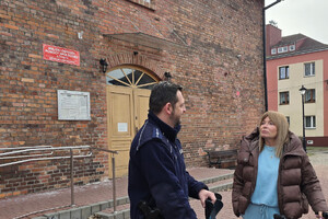 Na zdjęciu widoczny dzielnicowy oraz przedstawicielka Miejskiego Ośrodka Kultury w Zawierciu, której policjant przekazuje dwa wózki inwalidzkie oraz komplet kuli ortopedycznych.