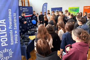 Policjanci przy stoisku profilaktycznym, prezentują uczniom policyjny sprzęt.