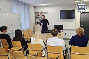 Policjant prezentuje sprzęt gościom na sali odpraw.