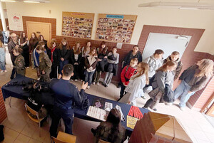 Policjant przy stoisku profilaktycznym podczas Dnia Otwartego szkoły. Wokół zgromadzeni są uczniowie. Na stolikach leżą materiały profilaktyczne oraz sprzęt policyjny.