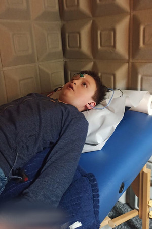 Na zdjęciu widać chłopca, który leży na specjalistycznym łóżku mając przytwierdzone elektrody w obrębie głowy.