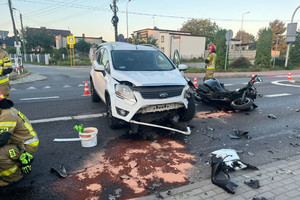 Na miejscu widać strażaków oraz opisywane miejsce zdarzenia z udziałem białego samochodu oraz motocykla.