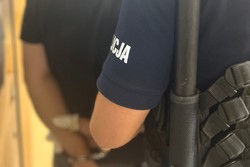 Na zdjęciu widać zatrzymanego mężczyznę, prowadzonego w kajdankach do celi przez policjanta.