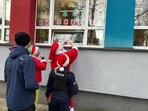 Na zdjęciu widać policjantów, mężczyznę ubranego w stój świętego mikołaja pod szkolnym oknem.