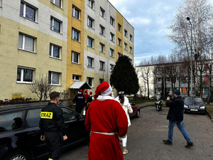 Na zdjęciu widać policjantów oraz osoby przebrane w kolorowe stroje, wchodzących do mieszkalnego bloku.