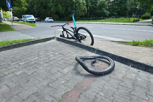 Na zdjęciu widać uszkodzony rower oraz samochody oraz drogę.
