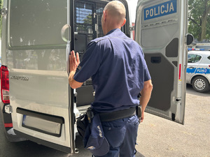 Na zdjęciu widać policjanta i srebrny pojazd służby konwojowej.